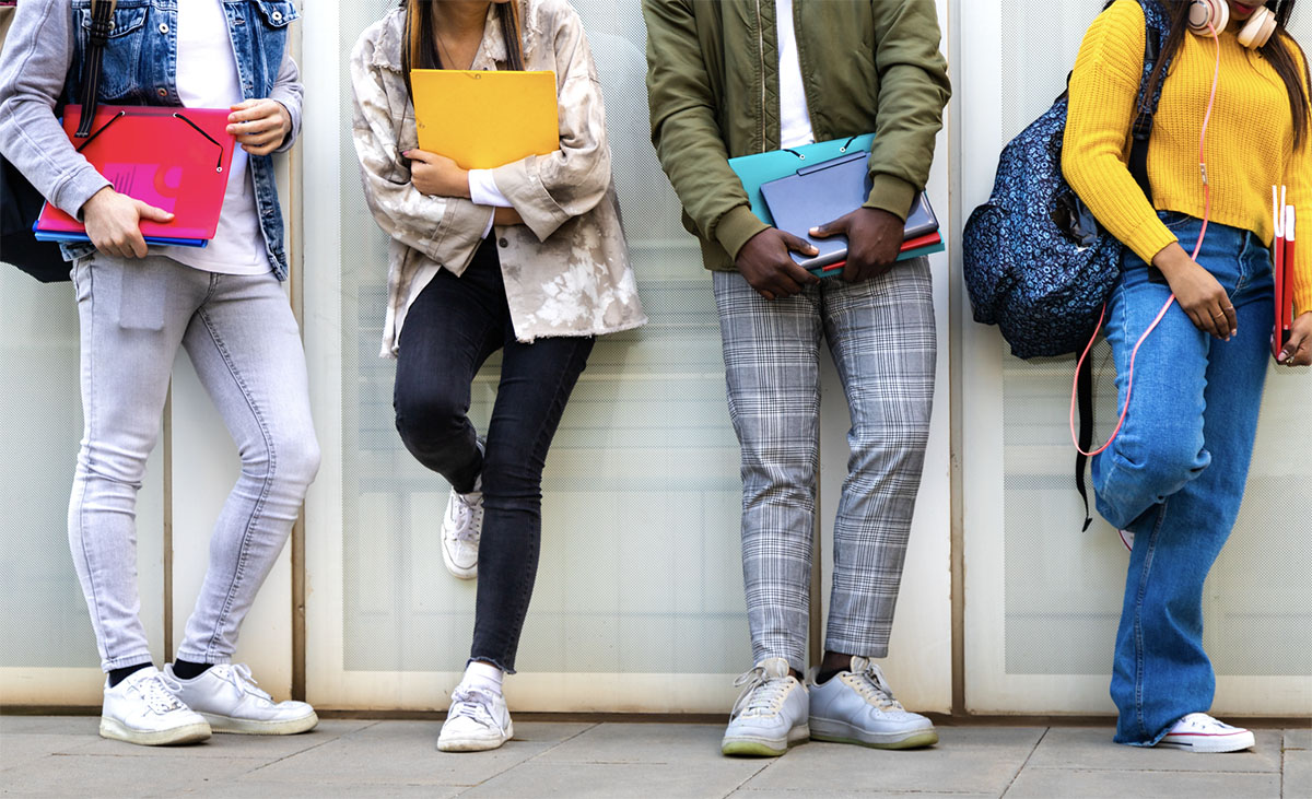 Group of multiracial teenage college students ready to go back to school standing against blue background wall. Higher education concept.