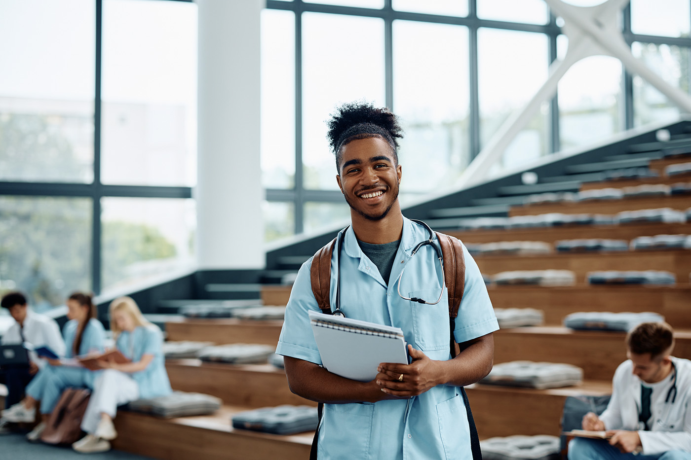 Happy African American student of medicine standing in amphitheater of medical university and looking at camera.
