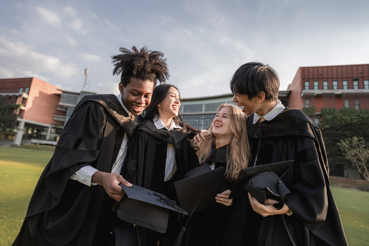 Group of international fresh graduates hugging and celebrating their achievements with wide smiles, laughing and sharing heartfelt words, reflecting on their journey and the challenges they overcame